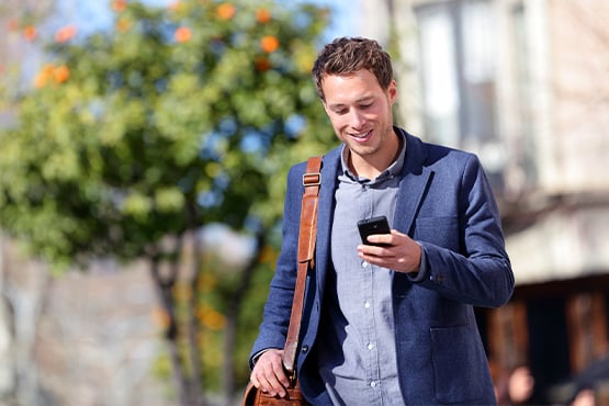 happy professional young man walks while looking at phone