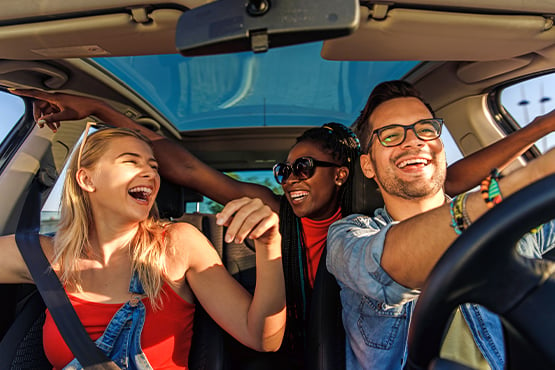 Three young adults laughing inside car on a road trip
