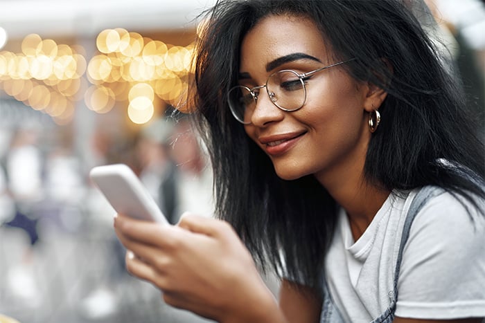 smiling young woman with glasses looks at phone and gets ready to transfer money