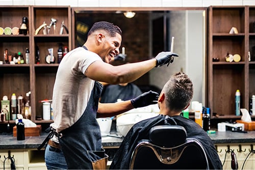 Laughing young barber shop owner, styling a gentleman’s hair in downtown Bismarck, ND