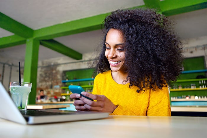 happy young woman in yellow sweater enjoys using mobile check deposit at table