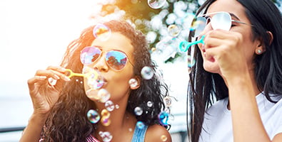 two young women wearing aviator sunglasses, blowing bubbles on a park bench in Fargo, ND
