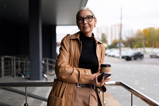 businesswoman in glasses and tan blazer in downtown Fargo, ND, checking her money market savings account balance on her phone