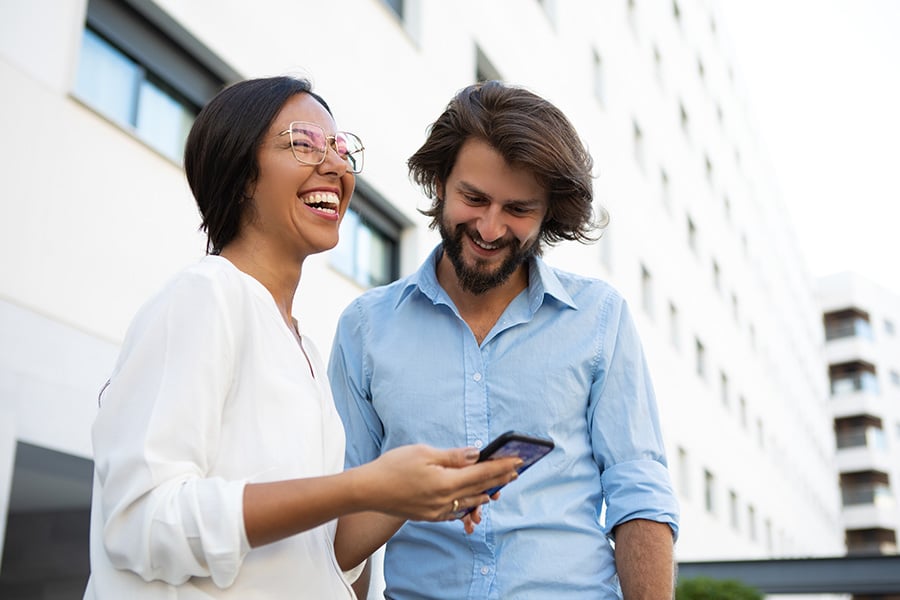 a female businessperson & male colleague happily view Gate City Bank’s new online & mobile banking resources on a smartphone