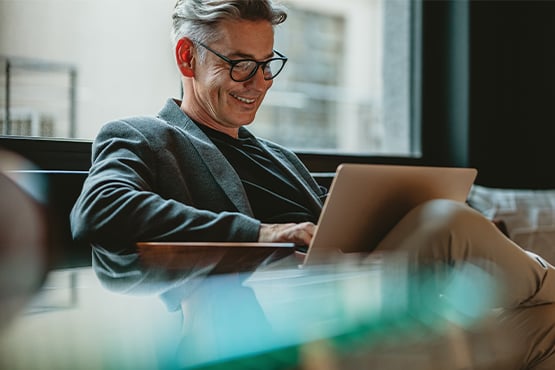 businessman in a gray suit jacket smiles while using his laptop to learn about Gate City Bank’s competitive business CDs