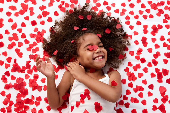 Giggling girl surrounded by red heart-shaped confetti, celebrating Giving Hearts Day in Fargo, ND