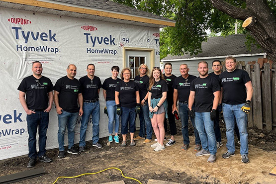 colleagues from Beyond Shelter wear matching shirts and pose for a photo in front of an ongoing affordable housing project