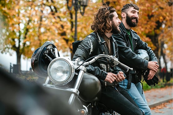 two male friends smile and lean on a motorcycle on a fall day after learning how to finance a motorcycle from Gate City Bank