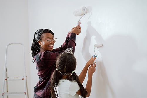 Smiling mom and her daughter holding foam rollers, painting a white room while remodeling their home in Fargo, ND