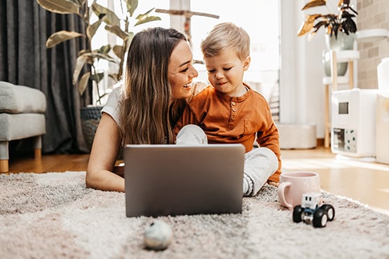 brunette mom with her young toddler, sitting on the floor together while she requests a free insurance quote on her laptop