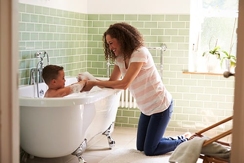 a happy mother kneels next to a tub to give her young son a bath after securing a home equity loan from Gate City Bank