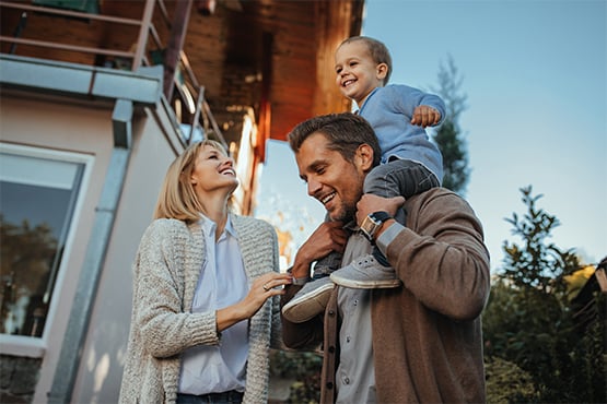 a dad carries his son on his shoulders and smiles with his wife after learning the benefits of buying vs building a house