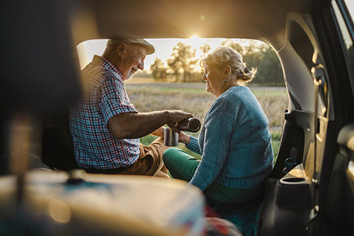 Senior couple at sunset, sitting in the back of their SUV and enjoying coffee together in rural ND