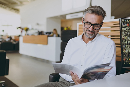 Silver-haired business owner with black-rimmed glasses, considering ways to add services to his car dealership in Grand Forks, ND