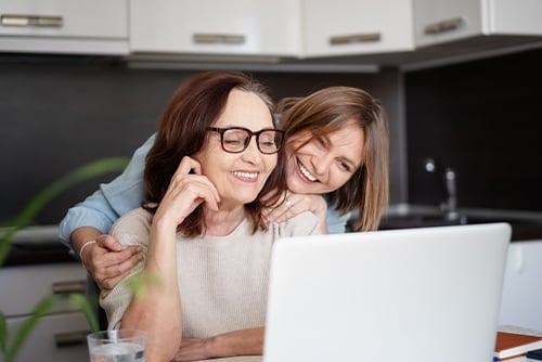 Senior woman with her beloved daughter, sitting at the kitchen table together while using reading free articles from Gate City Insurance