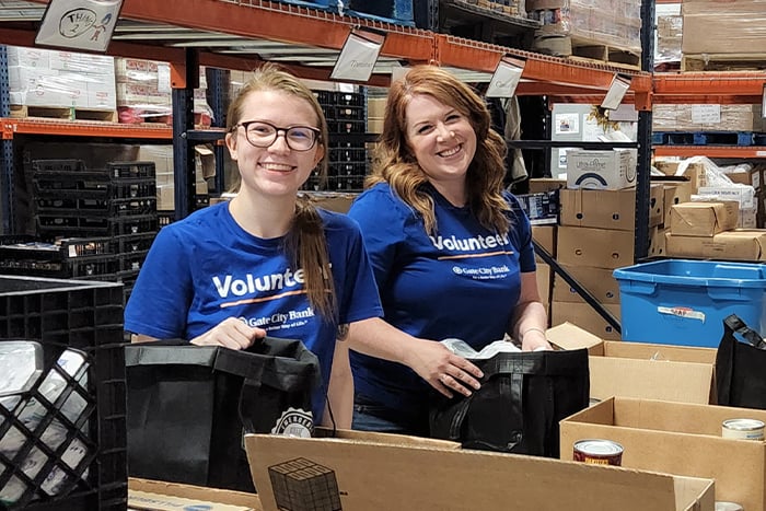 two Gate City Bank women volunteers smile while helping Emergency Food Pantry