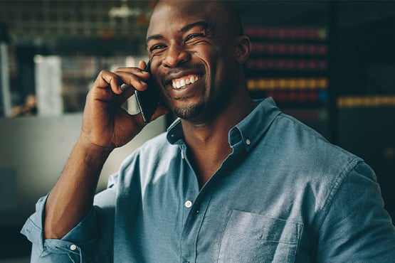 businessman in a blue chambray shirt in downtown Grand Forks, ND, smiling while talking on the phone with his business banker