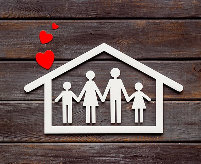 a white silhouette of a happy family in front of their new home with red hearts rising up and a wooden background