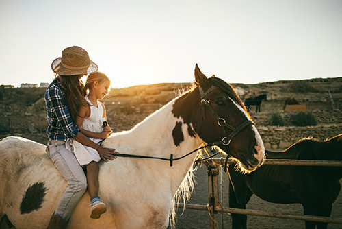 Mom and her young daughter riding bareback together on a paint horse at sunset on the edge of Hettinger, ND