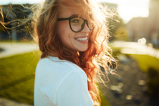 woman in sunshine with glasses turns to smile at the camera after receiving a loan with gate city bank