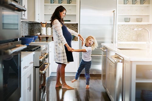 Laughing expecting mother and her daughter, twirling around together in the kitchen of their new Minnesota home