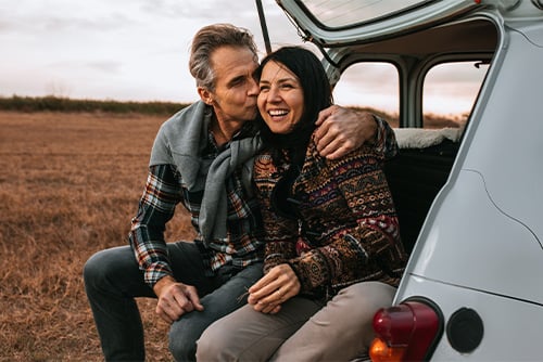 Happy fortysomething couple enjoying an autumn sunset, sitting in the back of a car on a dirt road outside of Williston, ND