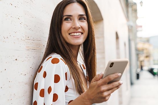 Happy brunette in a polka dot blouse, looking at the latest Gate City Bank checking account offers on her smartphone