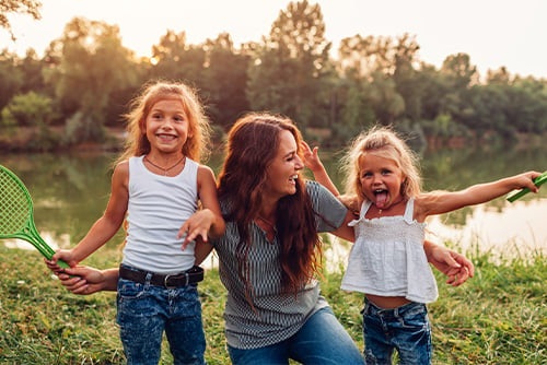 Laughing mom with her two young blond daughters, playing badminton on a summer day in Park River, ND