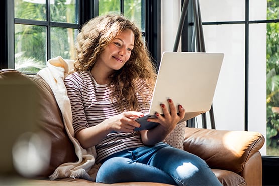 a young woman relaxes on the couch and uses her computer to run numbers with Gate City Bank’s mortgage calculators