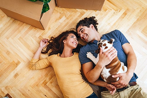 young woman smiling at her husband and bulldog puppy as they relax on the hardwood floor of their new home in Fargo, ND